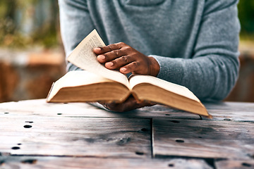 Image showing Hands, religion and a man reading the bible at a table outdoor in the park for faith or belief in god. Book, story and spiritual with a male christian sitting in the garden for learning or worship