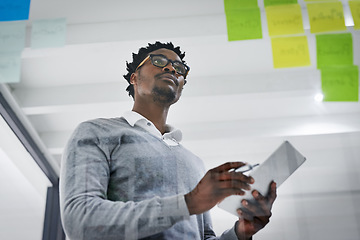 Image showing Business tablet, glass wall and black man brainstorming, strategy or research ideas in office. Sticky notes, planning and African male professional with technology for working, schedule and low angle