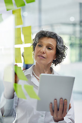 Image showing Glass wall, tablet and business woman writing, planning and strategy in office workplace. Sticky notes, brainstorming and senior female professional with technology for working, schedule and info.