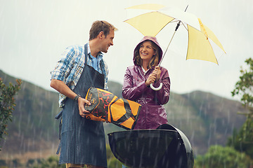 Image showing Man, woman and barbecue in rain with umbrella, charcoal or surprise on vacation with love in garden. Couple, outdoor and grill in storm, backyard or cooking in winter with helping hand, wind or smile