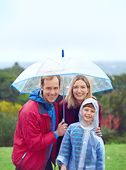Image showing Rain, outdoor and a happy family with umbrella for a portrait in nature for fun, happiness and quality time. Man, woman and boy child together for water drops and freedom while playing at a park