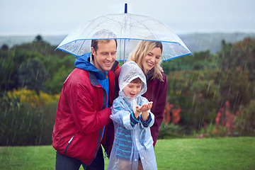 Image showing Rain, umbrella and a happy family outdoor in nature for fun, happiness and quality time. Man, woman and excited child together with hands to catch water drops while learning, playing or development