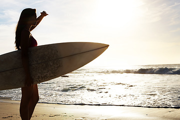 Image showing Silhouette, woman surfer on beach with sea and exercise outdoor with surfboard to surf in nature. Sport, shadow and sun with female person looking at ocean waves view with surfing and fitness