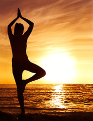 Image showing Silhouette, sunset and woman in tree pose with yoga on the beach, orange sky and fitness outdoor. Meditation, wellness and peace in nature with shadow, female yogi person and pilates by the ocean