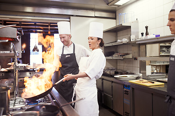 Image showing Chef, woman and fire with frying pan in kitchen, catering service and prepare food for fine dining. Professional, cooking and person saute, fry with flame and cook delicious meal in restaurant.