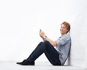 Image showing Man, phone and floor with space by wall in portrait, communication or texting app with smile. Young businessman, entrepreneur and happiness sitting with smartphone in mock up for social media chat