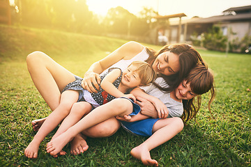 Image showing Mother, children and hug playing on grass for fun bonding in the sun outside their house in nature. Happy mom hugging kids on garden floor outdoors in playful, joy and happiness of family together