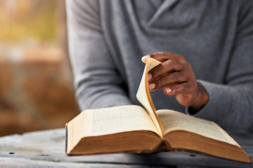 Image showing Hands, spiritual and a man reading the bible at a table outdoor in the park for faith or belief in god. Book, story and religion with a male christian sitting in the garden for learning or worship