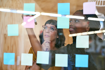 Image showing Business people, thinking and planning with notes in a creative office for designer project. Women team together for collaboration, teamwork and ideas on a glass wall with color paper and diversity