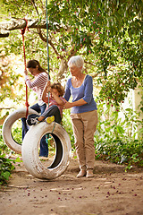 Image showing Senior woman, garden and grandma pushing her grandchildren on a tyre swing or holidays and having fun in summer. Excited, grandkids and elderly woman outdoors on jungle gym or on sunny day at a park