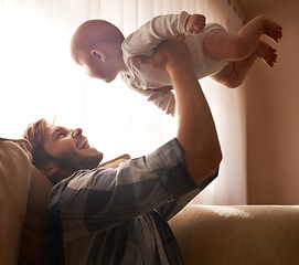 Image showing Funny, father and lifting baby on sofa in home living room, playing or bonding together. Happy, care and dad holding infant, newborn or child on couch in lounge, having fun and enjoying quality time.