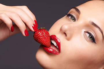 Image showing Makeup, portrait and woman with a strawberry in a studio with red nails and lipstick cosmetics. Health, wellness and closeup of a female model eating fruit for nutrition isolated by a gray background