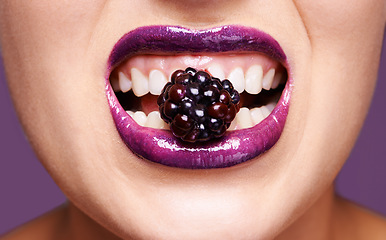 Image showing Woman lips, purple lipstick with berry and makeup, shine and creativity with beauty isolated on studio background. Closeup of fruit between female model teeth, cosmetic product and cosmetology