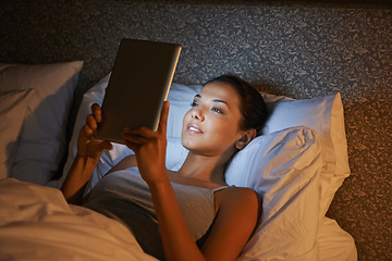 Image showing Woman, night and bed for reading on tablet, website or social media app to relax in home, hotel or apartment. Girl, mobile touchscreen and happy with ebook, movie or video on internet in bedroom