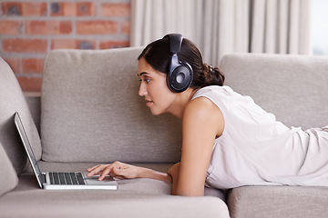 Image showing Woman, laptop and lying on sofa with headphones for streaming, music or search for web video in home. Girl, computer or scrolling for movie, podcast or audio on internet to relax on living room couch