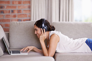 Image showing Woman, laptop and lying on couch with headphones for streaming, music and search for web video in home. Girl, smile and scrolling for movie, podcast or meme on internet to relax on sofa with computer