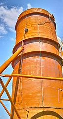 Image showing A tall silo water tower against a blue sky background from below. An orange storage tank for the farming or agriculture industry used for large scale grain or wheat production on a farm