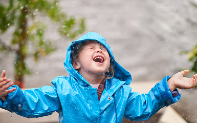 Image showing Winter, rain jacket and a girl playing in the weather outdoor alone, having fun during the cold season. Children, water or wet with an adorable little female kid standing arms outstretched outside