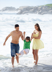 Image showing Family, summer and swinging child at beach for fun, travel or holiday with a smile in water. A man, woman and kid or son playing together on vacation at sea with waves, love and happiness outdoor