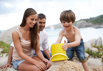 Image showing Family, child and sand castle at beach in summer for fun, travel or holiday with a smile. A man, woman and excited kid playing together on vacation at sea with a toy bucket, development and happiness