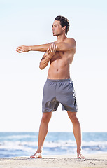 Image showing Fitness, man and stretching arms on beach getting ready for body exercise, workout or training in nature. Fit, active or muscular male person in warm up arm stretch for cardio or exercising by ocean