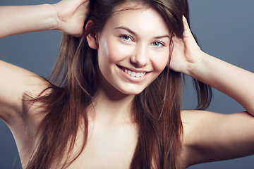 Image showing Face, smile and beauty portrait of a woman in studio with natural makeup, hands in hair care and cosmetics. Headshot of aesthetic female model on a blue background for glow, skincare or facial health