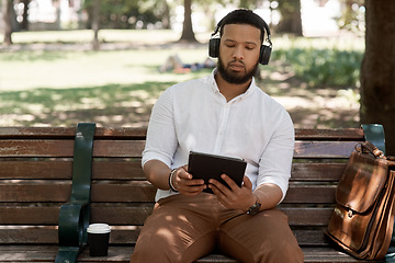 Image showing Business man, headphones and outdoor with a tablet on a park bench for a break with internet. Male digital nomad and person in nature while streaming and listening to music on a audio app to relax