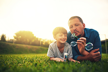 Image showing Garden, family and father and boy with bubble for quality time, bonding and having fun together. Summer, parenthood and happy dad and child blowing bubbles in park for playing, happiness and relaxing