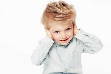 Image showing Kid, happy and cover ears in portrait with shirt in studio background with cute face. Young child with smile hear loud noise while sensitive to sound in childhood as emoji on white, isolated backdrop