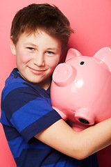 Image showing Happy boy, portrait smile and piggy bank for investment, savings or coins against a pink background. Little child or kid holding piggybank and smiling for financial freedom, money or growth in profit