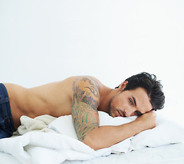 Image showing Thinking, relax and topless with a sexy man on a bed, lying in studio on a white background. Tattoo, idea and shirtless with a handsome young male model posing in a bedroom for sensuality or desire