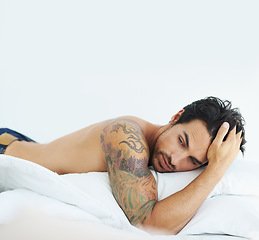 Image showing Idea, relax and shirtless with a sexy man on a bed, lying in studio on a white background. Tattoo, thinking and topless with a handsome young male model posing in a bedroom for sensuality or desire