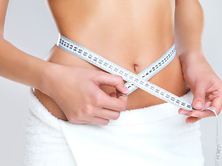 Image showing Woman, hands and tape measure on stomach for lose weight, diet or slim body against a grey studio background. Hand of female person or model measuring waist in weightloss, results or healthy wellness