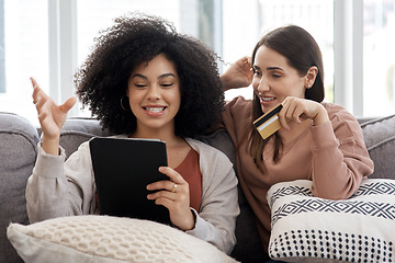 Image showing Tablet, credit card and online shopping with woman friends on a sofa in the living room of their home together. Ecommerce, technology and sale with female roommates browsing for deals on the internet