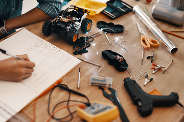 Image showing Engineering, person hand with notebook for homework and stationary or robot toys on desk at home. Technology, education or creative and male child writing or research information with pen in book