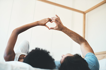 Image showing Interracial couple, hands and heart emoji in bed for morning, love or care relaxing together at home. Man and woman lying in bedroom with touching hand for loving symbol, sign or gesture at the house