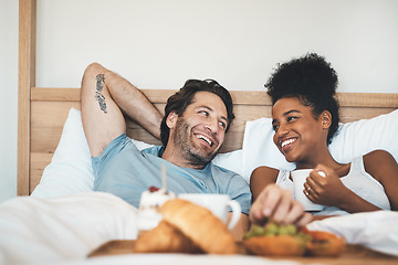 Image showing Happy interracial couple, bed and breakfast in relax for morning, bonding or relationship at home. Man and woman smiling with food, coffee or meal relaxing on holiday or weekend together in bedroom