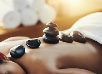 Image showing Woman, hot rocks and massage on back at spa for skincare, beauty or body treatment at resort. Calm female lying on bed with heated rock pile for healthy physical therapy, zen or wellness at salon