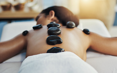 Image showing Woman, relax and stone massage at spa for skincare, beauty or body treatment on bed at resort. Calm female lying in relaxation with hot rocks or pile on back in therapy, zen or wellness at salon