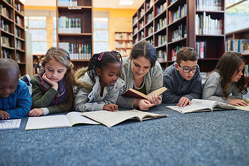 Image showing Education, teacher with children in library and lying on the floor of elementary school. Studying or knowledge with books, diversity and young students with woman reading textbook or notebook.