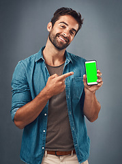Image showing Happy man, phone and pointing to mockup green screen for advertising against a grey studio background. Portrait of male person smiling and showing smartphone display or chromakey for advertisement