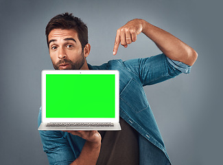 Image showing Man, laptop and pointing on mockup green screen for advertising or marketing against a grey studio background. Portrait of male person showing computer display, chromakey or mock up for advertisement