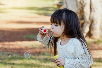 Image showing Nature, outdoor and girl blowing bubbles, freedom and playing for fun, development and happiness. Female child, kid and young person in the park, soap and game with bubble wand, growth and vacation