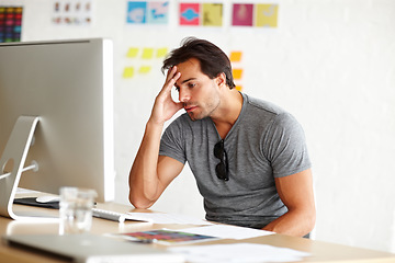 Image showing Suffering from writers block. A handsome man sitting at a desk and looking at a computer screen with head rested on his hand.