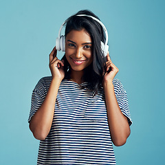 Image showing Woman, portrait and headphones with music in studio with happiness and web audio. Blue background, Indian female person and young model listening, hearing and streaming a song with smile and online