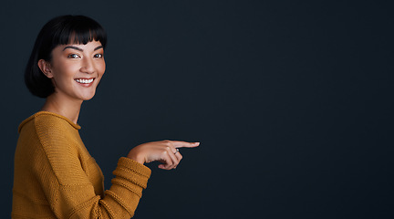 Image showing Woman is pointing, marketing and mockup space with portrait, smile and promo isolated on dark background. Young female person, happy ambassador and branding with advertising and show in studio