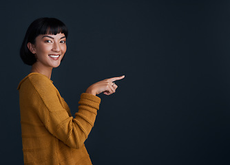 Image showing Woman is pointing, advertising and mockup space with portrait, smile and promo isolated on dark background. Happy female person, ambassador and branding with marketing and presentation in studio