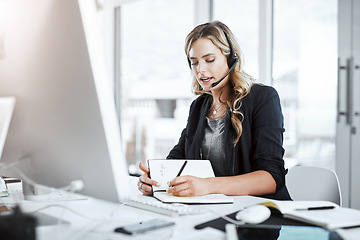 Image showing Woman with headset, call center and writing in notebook, notes and phone call with communication and CRM. Customer service, telemarketing and tech support with female consultant at desk with agenda