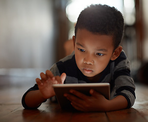 Image showing Little boy, browsing and on digital tablet or playing games or streaming video on the internet and lying on the floor at home on bokeh. Technology, device and male child downloading app or reading