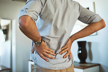 Image showing Hands, back pain and injury with a man standing in the living room of his home, holding his spine in discomfort. Health, medical and anatomy with a male person in a house feeling a muscle cramp